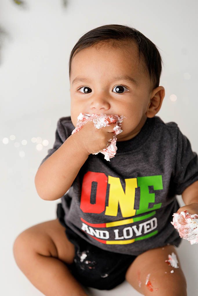 Baby boy in ONE AND LOVED shirt eating cake during first birthday cake smash photo session by Lake Elsinore 1st birthday photographer.