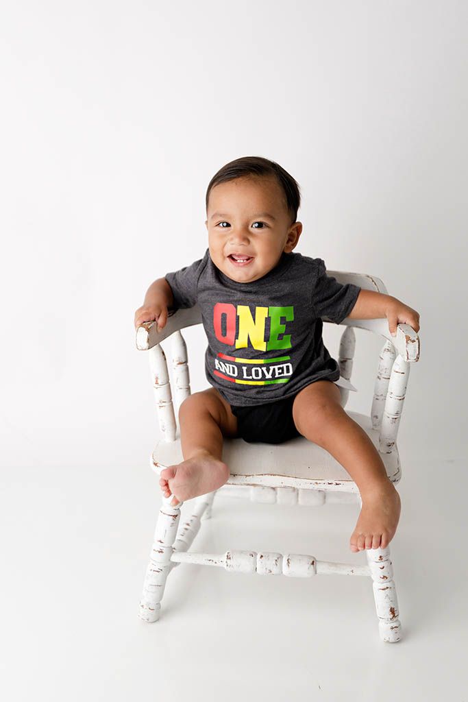 Smiling baby in a white chair wearing ONE AND LOVED shirt, celebrating his first birthday by Lake Elsinore 1st birthday photogragrapher.