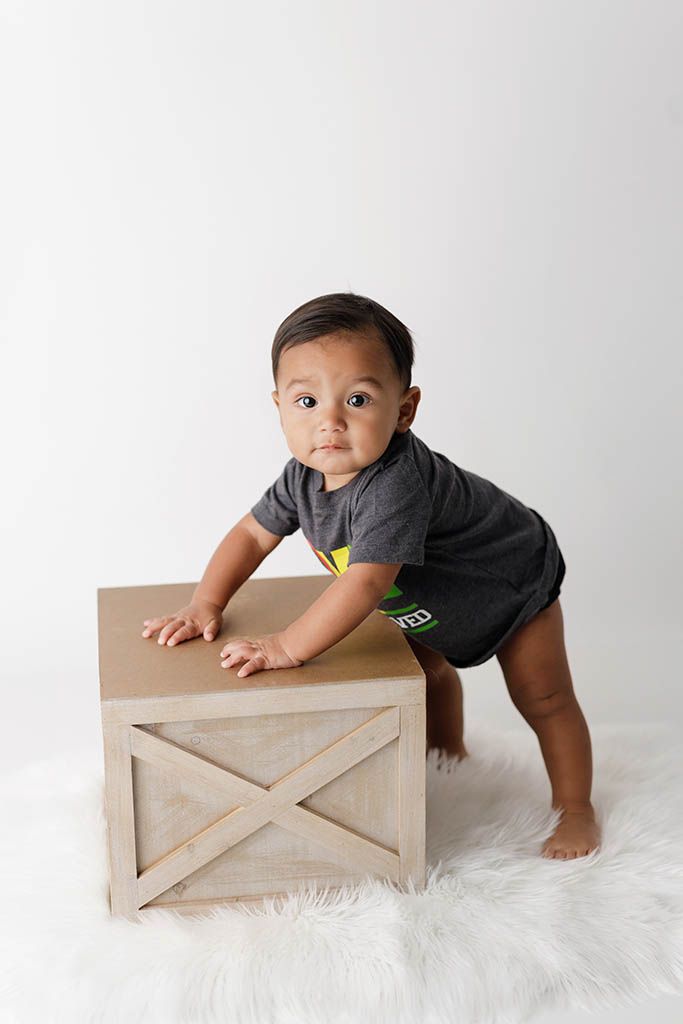 Adorable baby pulling up to stand on a wooden crate on white fur rug by professional Lake Elsinore 1st birthday photographer.