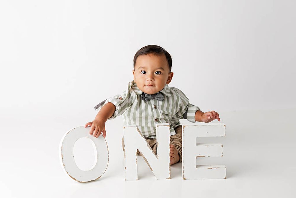 Baby boy holding white ONE letters for first birthday photo session by professional Lake Elsinore 1st birthday photographer.