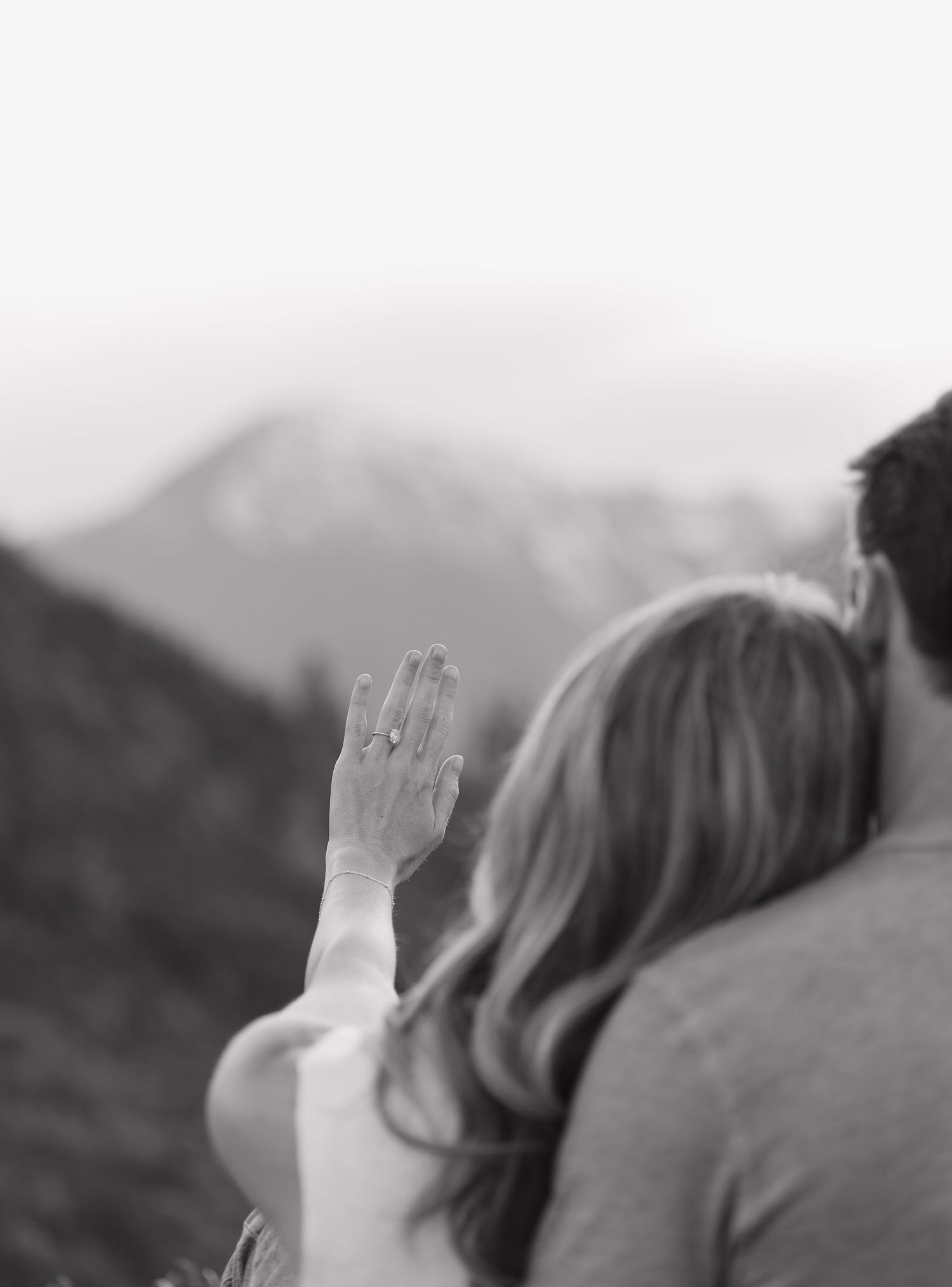 A person holds their hand up against a blurred mountain landscape background in black and white.