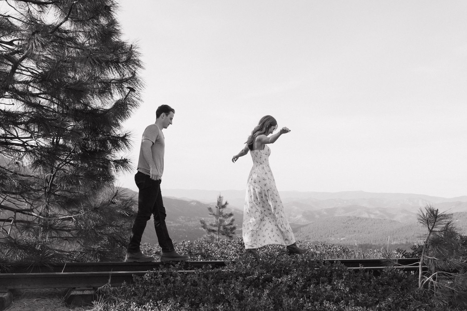 A black and white photo sequence shows a person walking across a log bridge over a scenic mountain landscape.