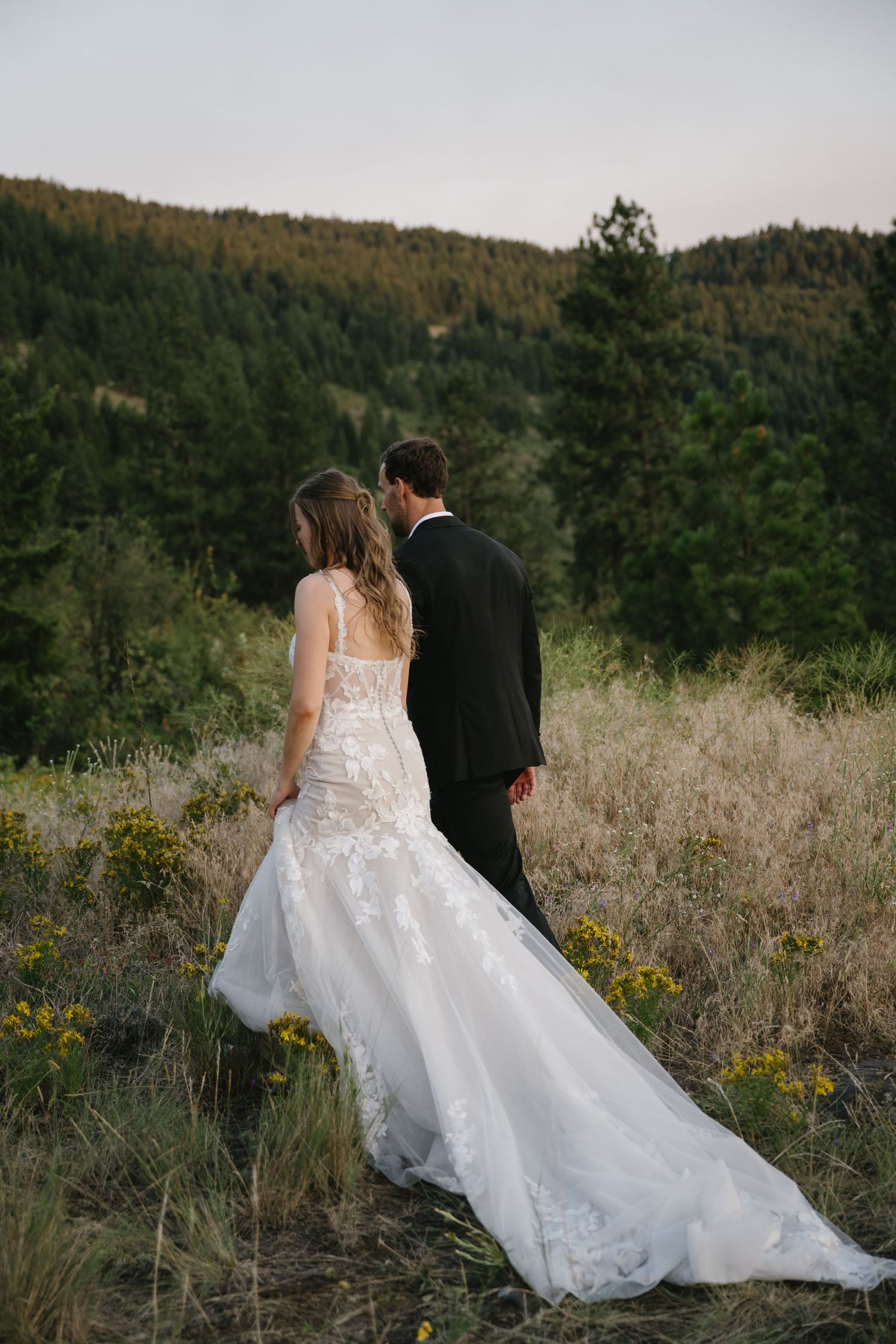 Bride and groom dancing on hilltop at golden sunset with sweeping mountain valley views.