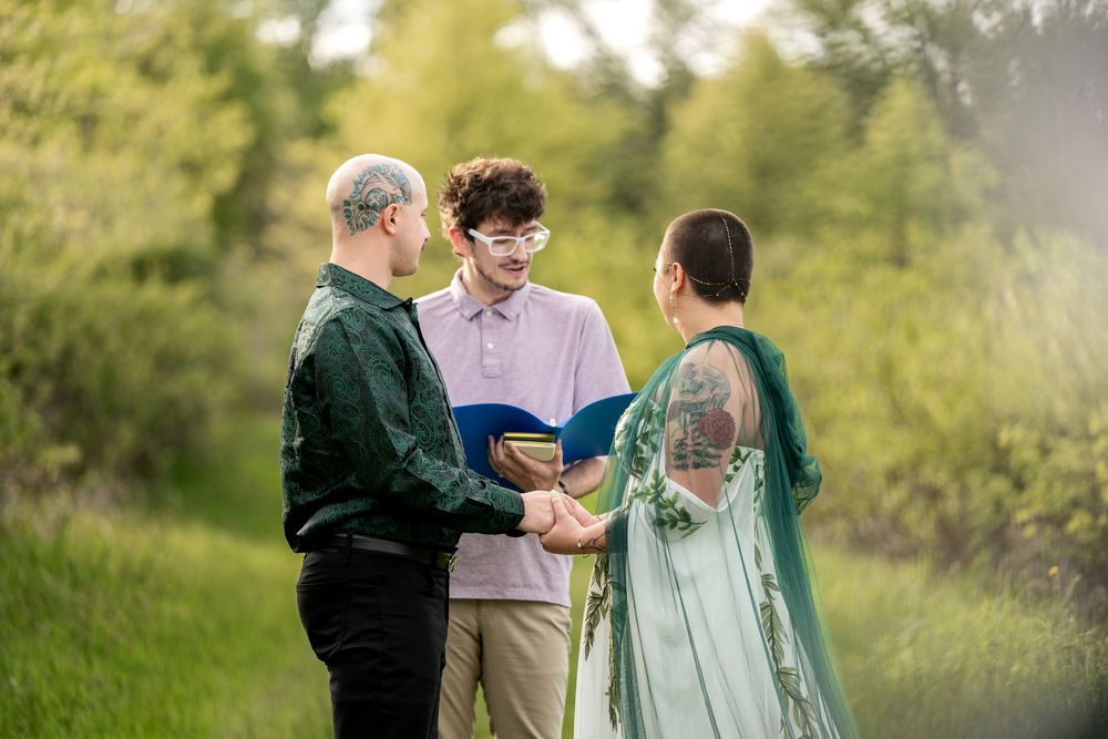 Outdoor wedding ceremony with couple exchanging vows before an officiant in a lush green setting.