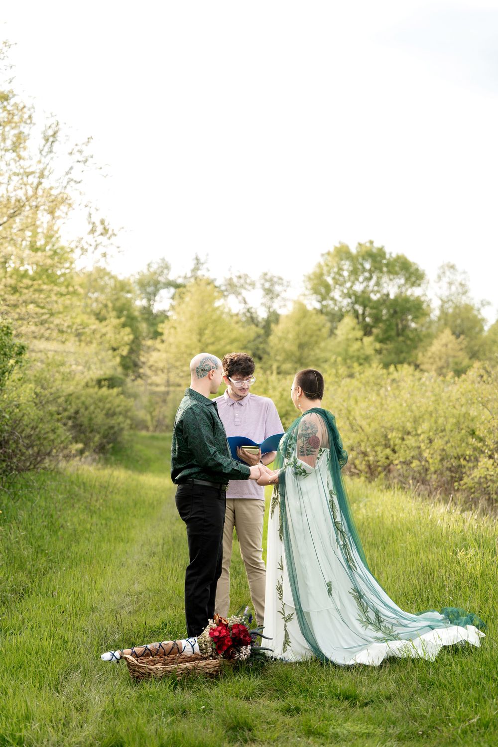 Outdoor wedding ceremony with couple exchanging vows before officiant in a scenic green meadow.