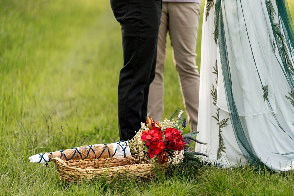 Wedding bouquet of red flowers in a wicker basket on green grass near couple.