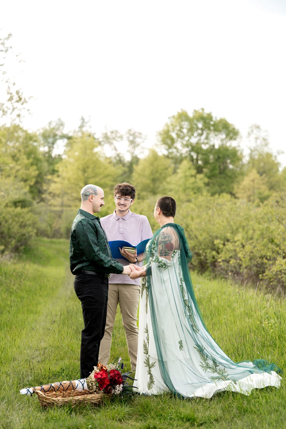 Outdoor elopement ceremony with couple exchanging vows with officiant in green meadow at golden hour.