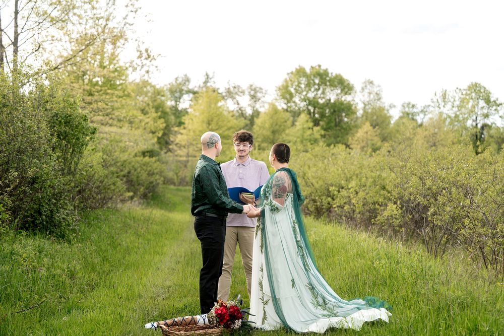 Intimate outdoor elopement ceremony with couple exchanging vows before officiant in lush greenery.