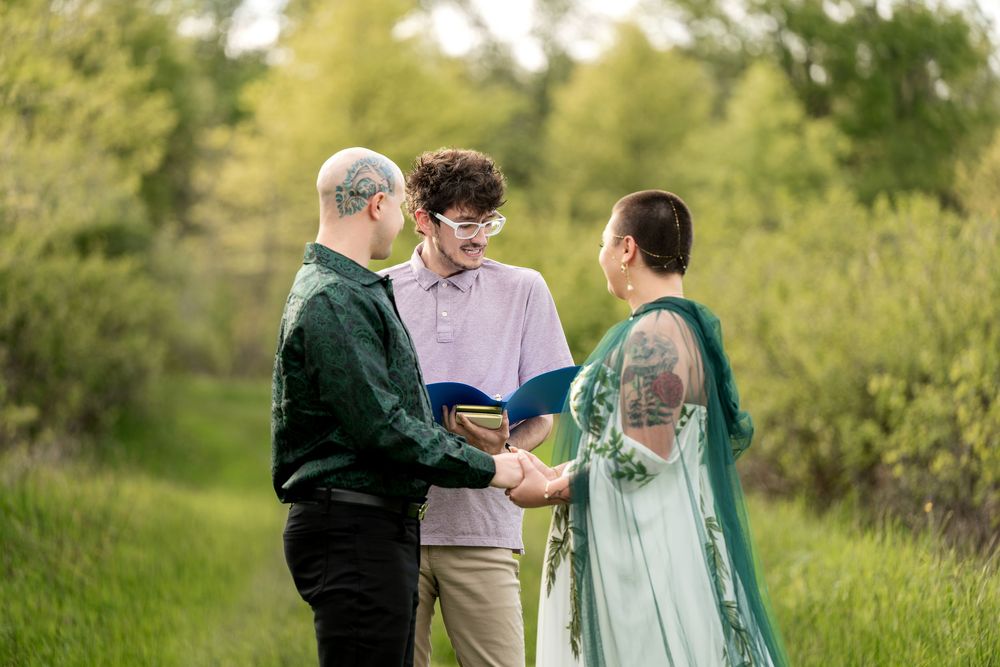 Outdoor wedding ceremony with couple holding hands before an officiant in a green meadow.
