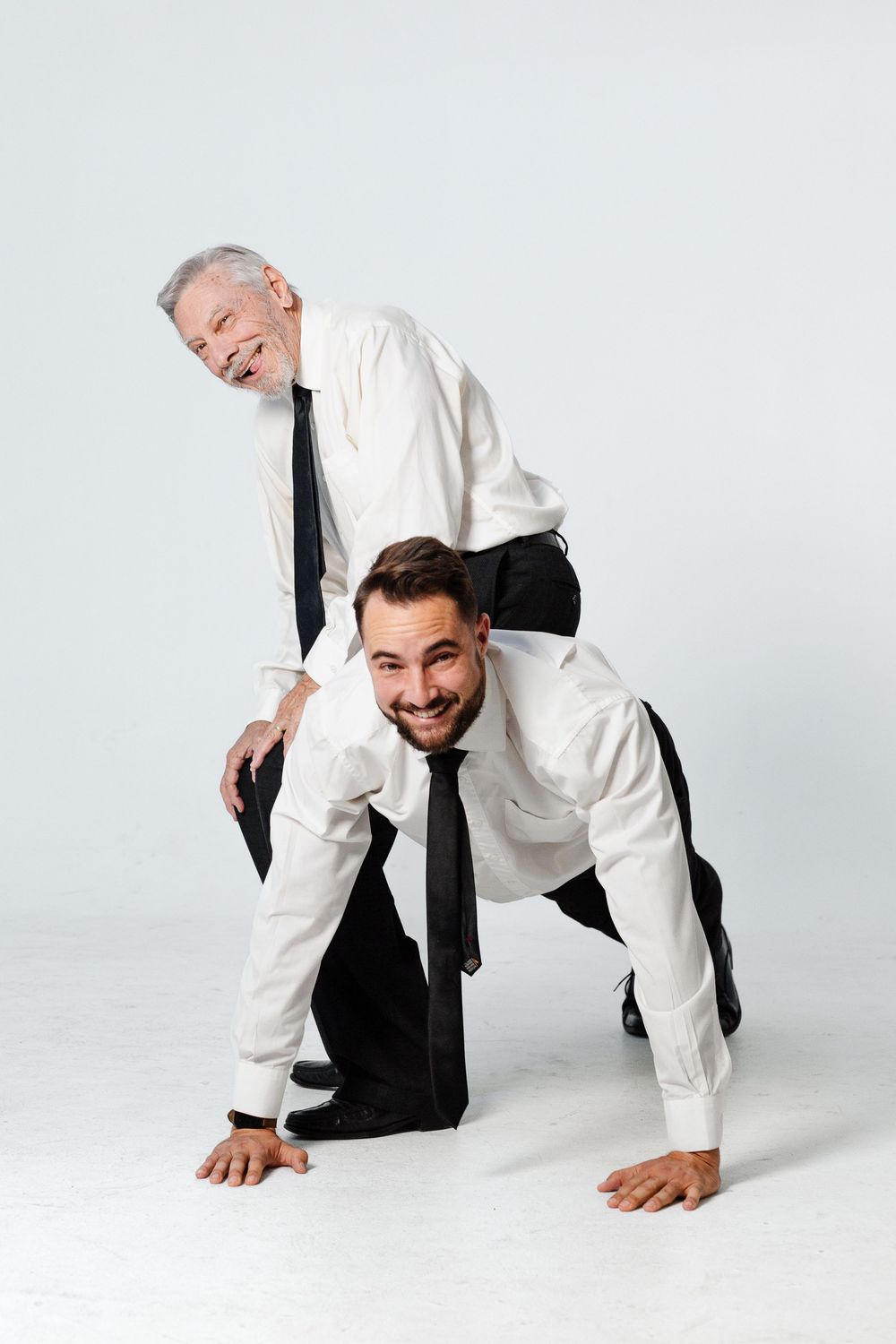 Two businessmen in white shirts and ties playfully pose with older man riding on younger mans back.
