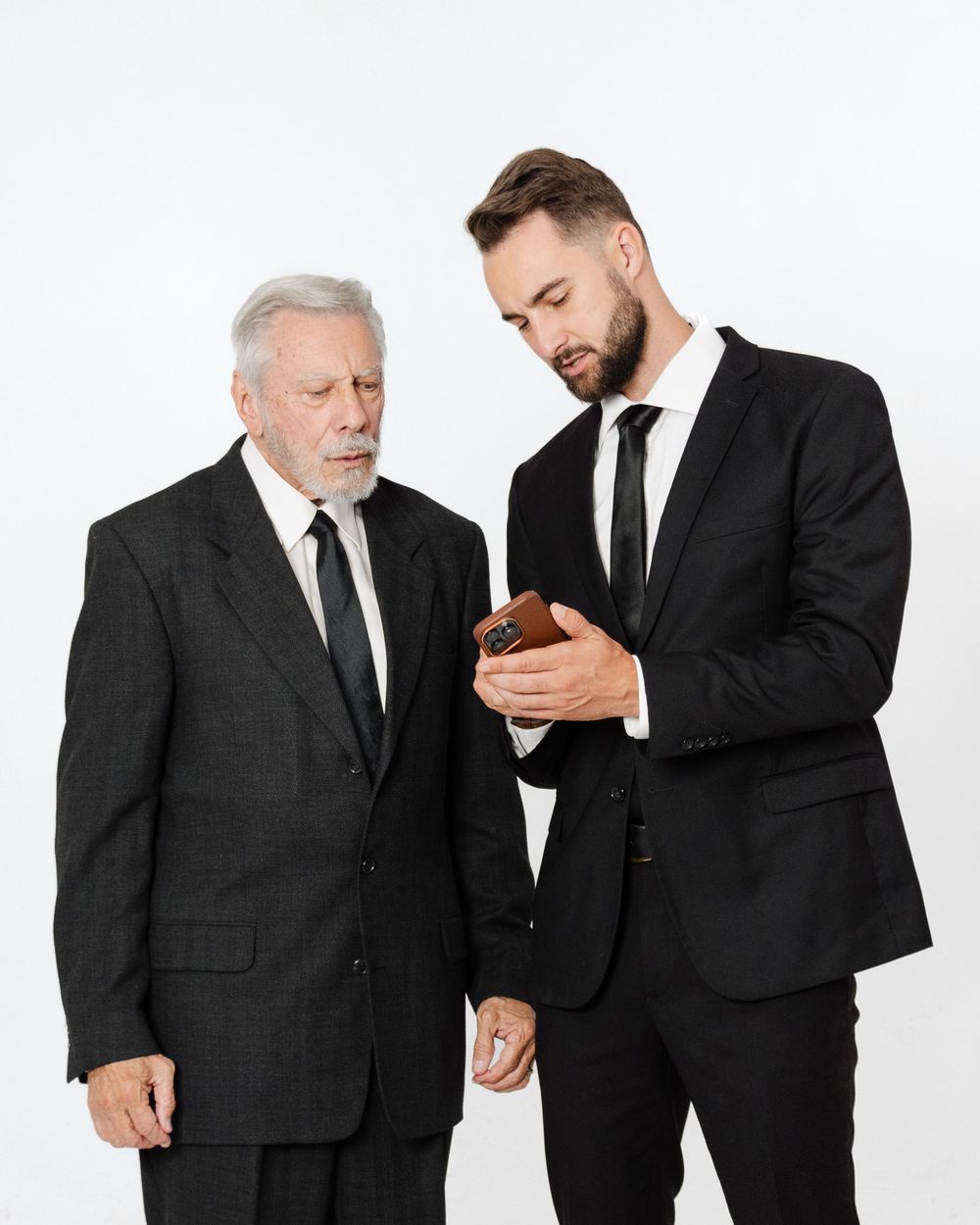 Two businessmen in black suits reviewing content on a smartphone against a white background.