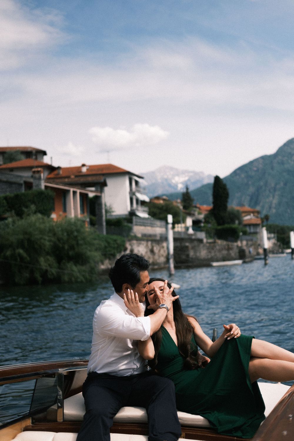 Romantic couple sharing a tender moment on a boat at Lake Como, Italy, with mountain backdrop.
