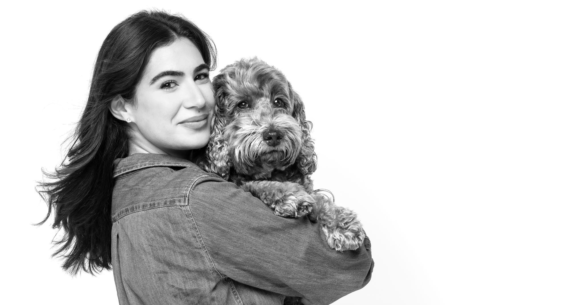 Black and white photo of a smiling woman holding a fluffy goldendoodle dog, posing together in a casual denim jacket.