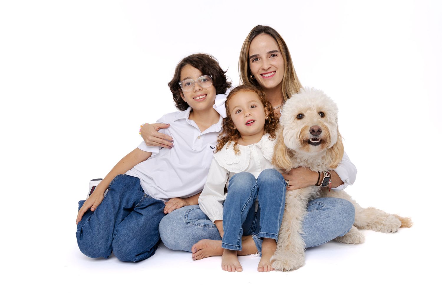 A happy family with two children and a fluffy goldendoodle dog posing together on a white background.