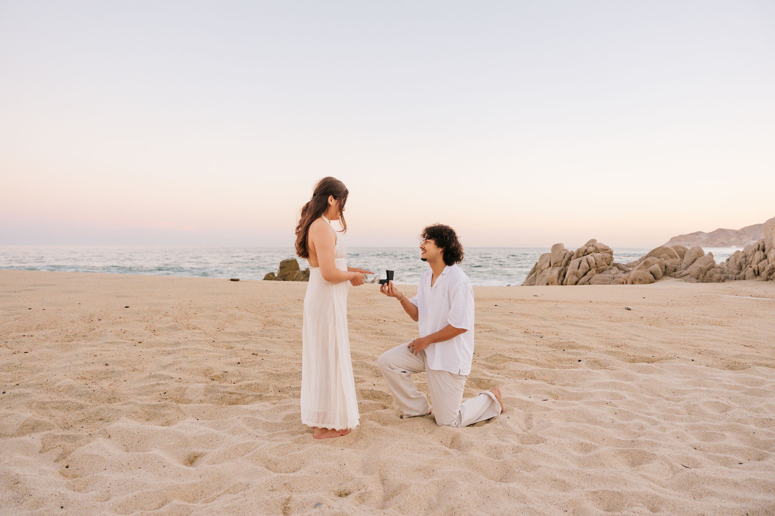 Man proposing to woman on sandy beach at sunset in Cabo San Lucas.
