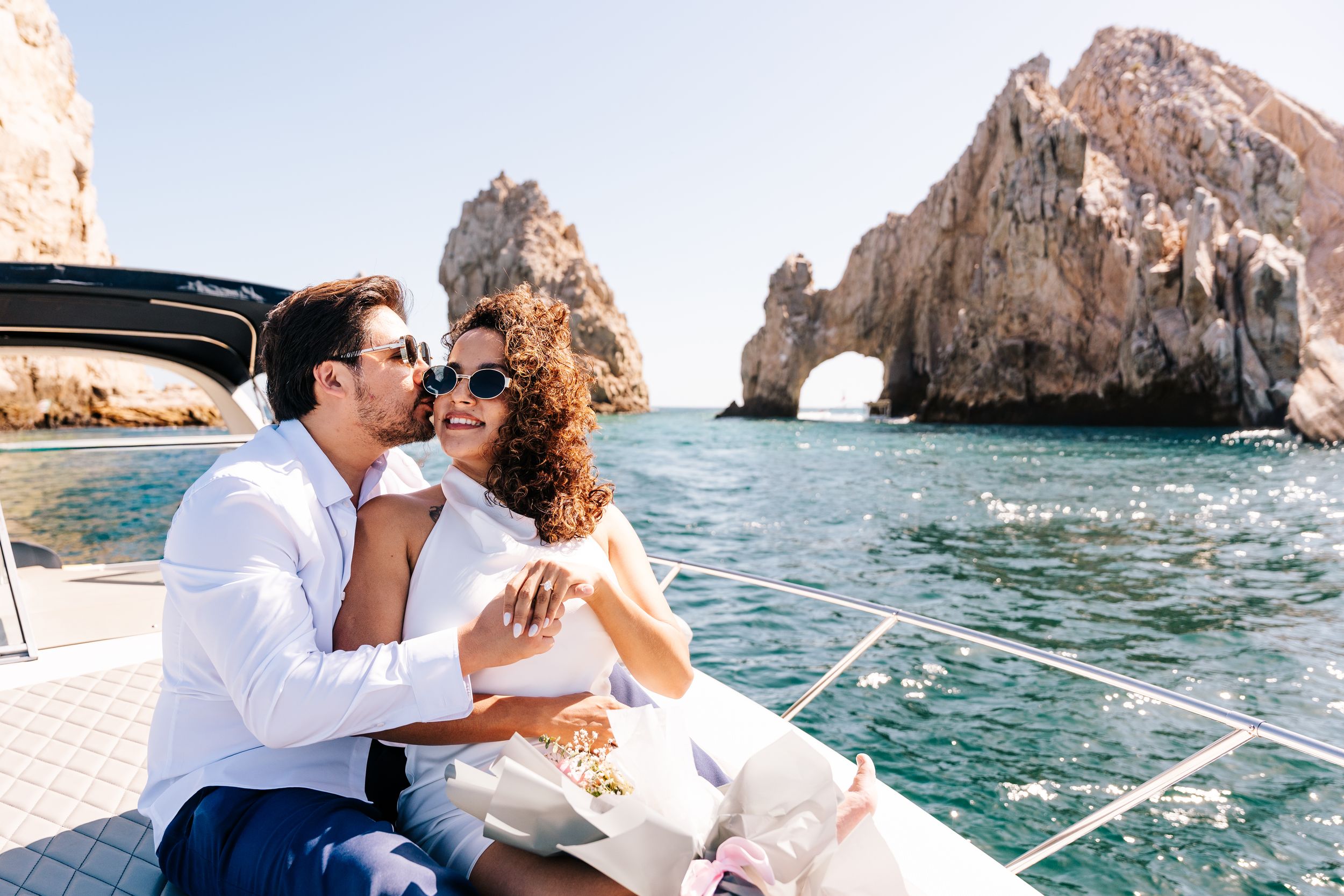 Couple relaxing on a luxury yacht near Los Cabos arch rock formation on a sunny day.