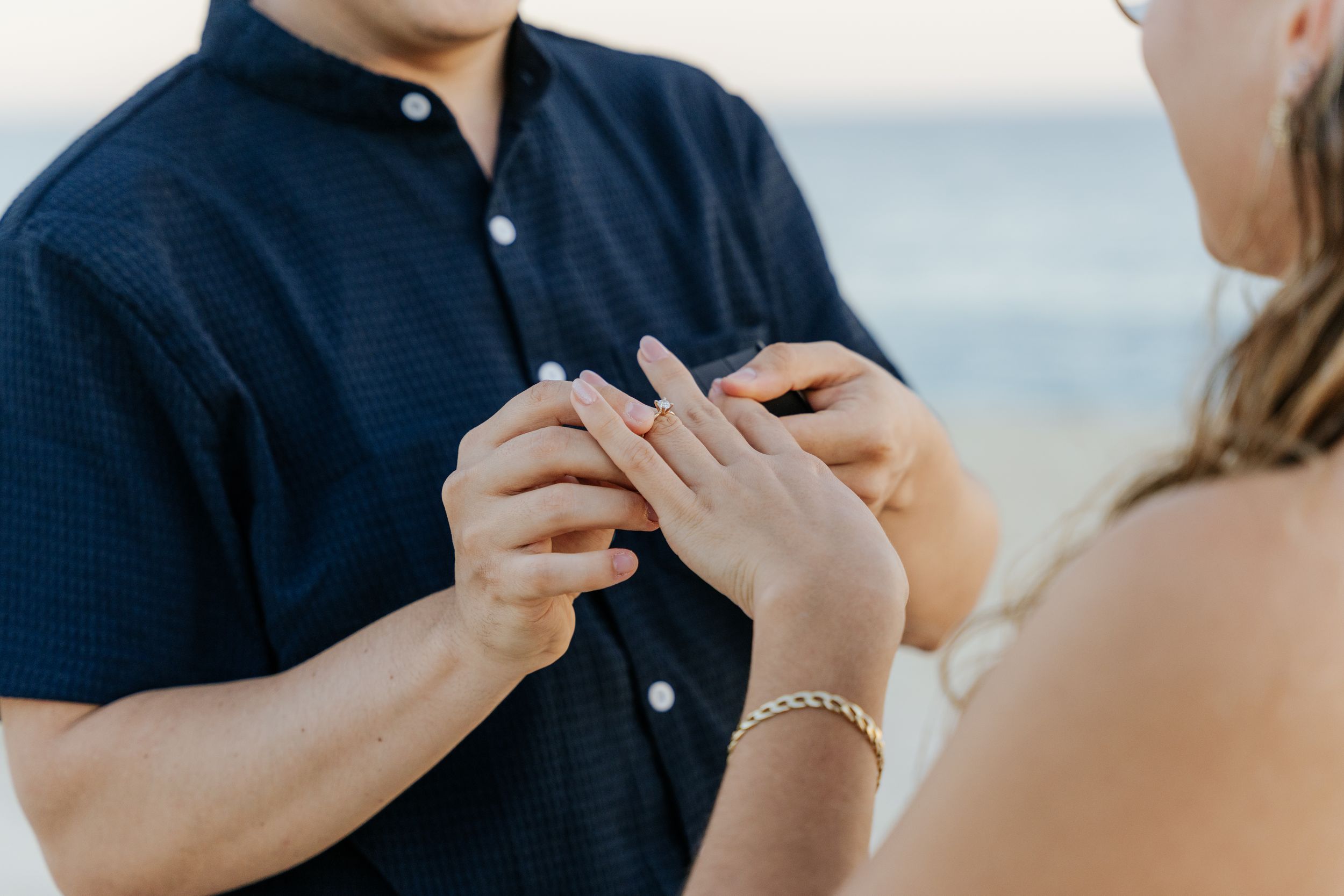 Couple exchanging rings on a beach during an outdoor wedding ceremony, with ocean in the background.