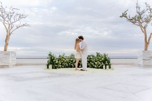 Couple sharing a romantic kiss at an outdoor wedding ceremony with floral arrangements and ocean backdrop.