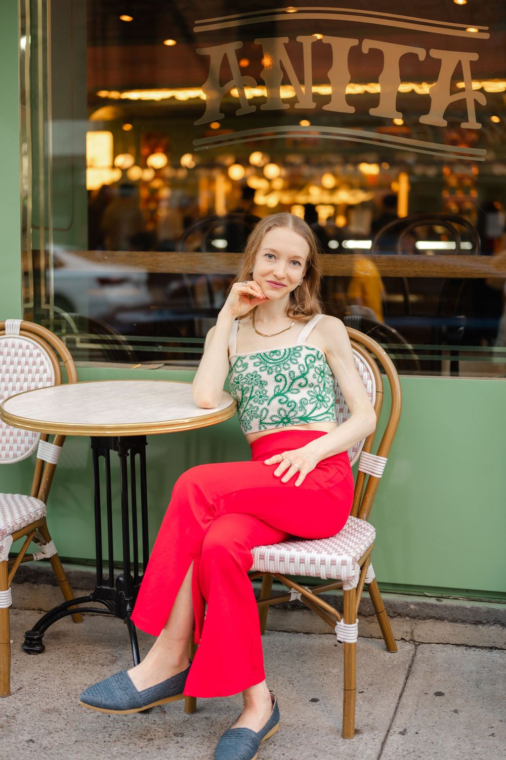 Young woman in green embroidered crop top and red wide-leg pants sitting outside cafe Anita.