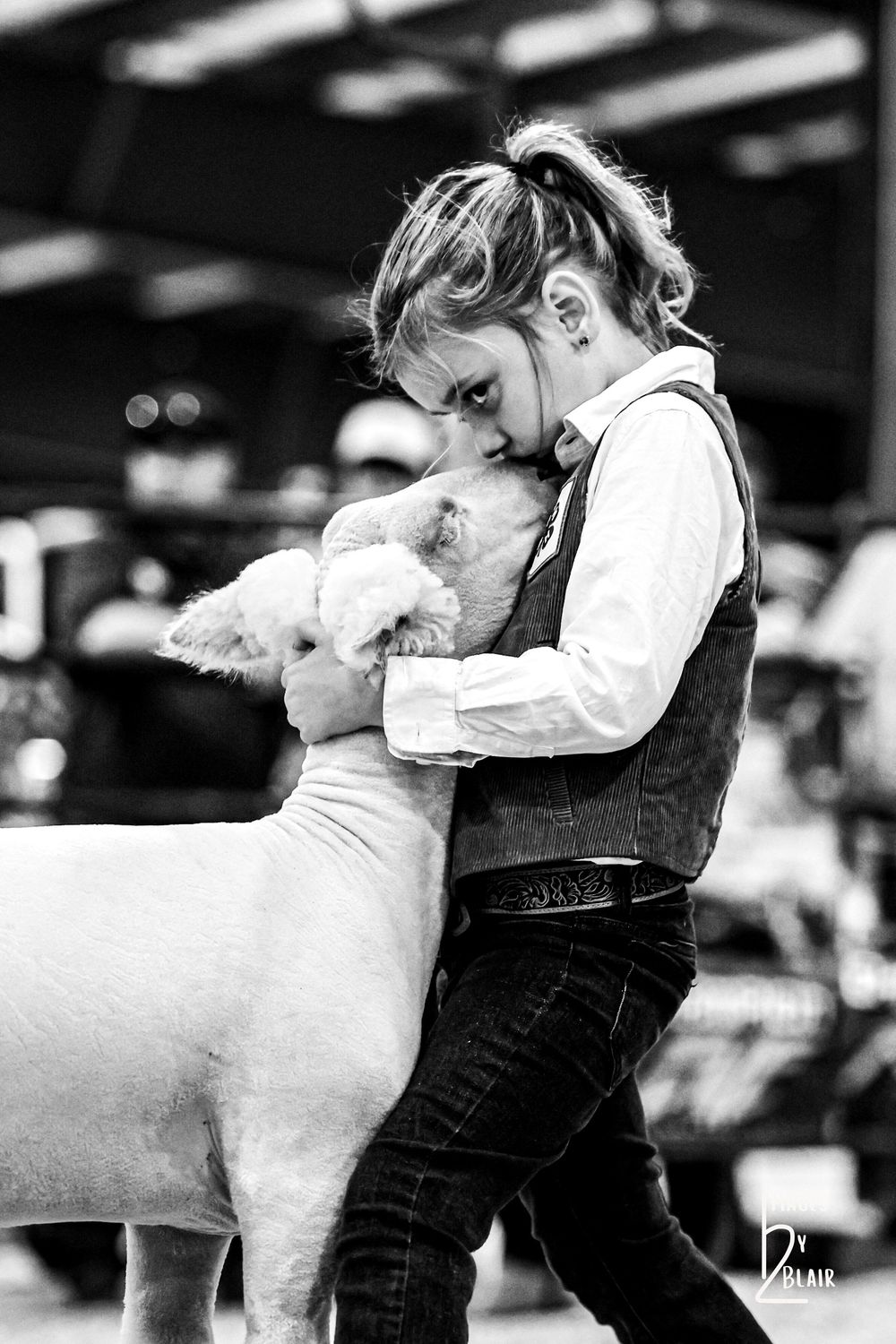 Young girl in vest hugging a white lamb at a livestock show, black and white photography.