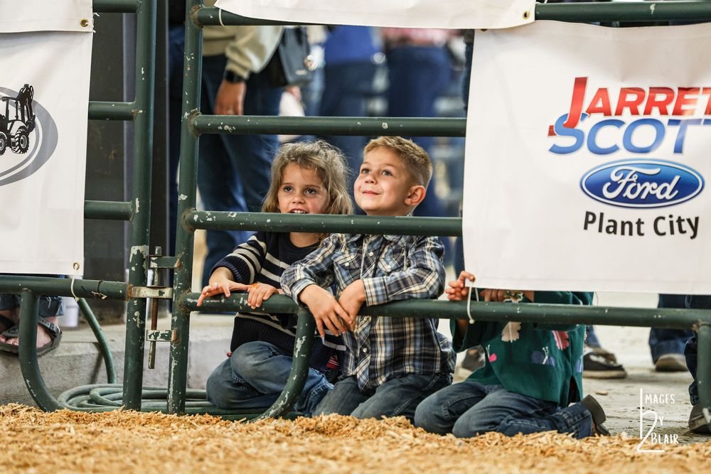 Two children watching a rodeo event from behind metal gates at Jarrett Scott Ford arena in Plant City.