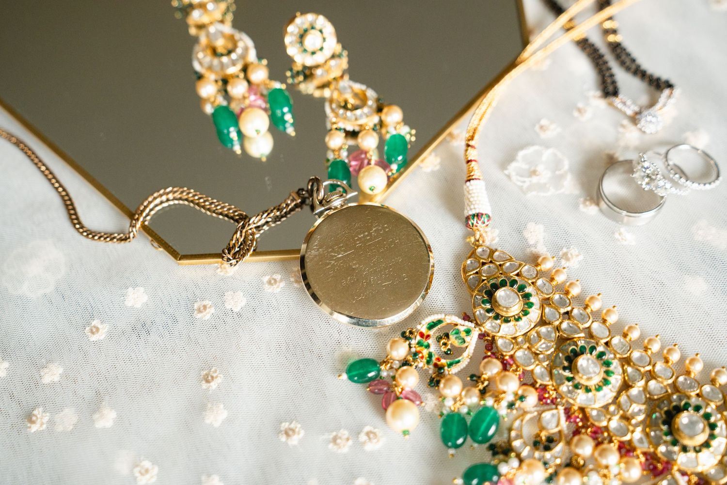 Elegant Indian bridal jewelry set featuring gold necklace, green gemstone earrings, pearl maang tikka, and silver ring.