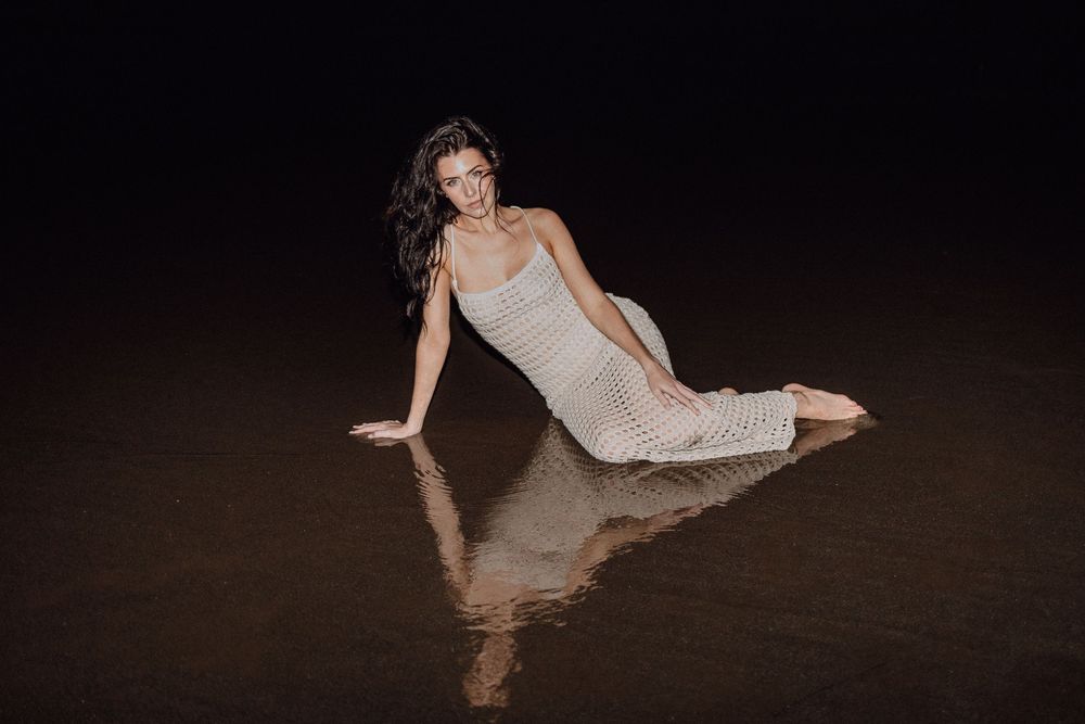 Woman in white dress posing gracefully on reflective wet surface at night.