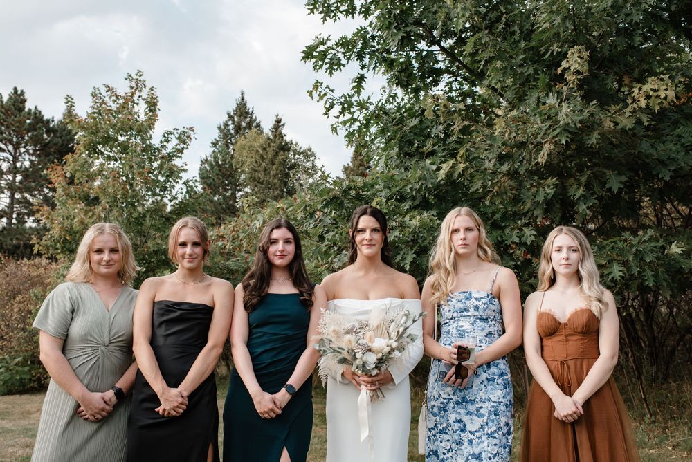 Bride poses with five bridesmaids in mismatched dresses outdoors at a garden wedding.