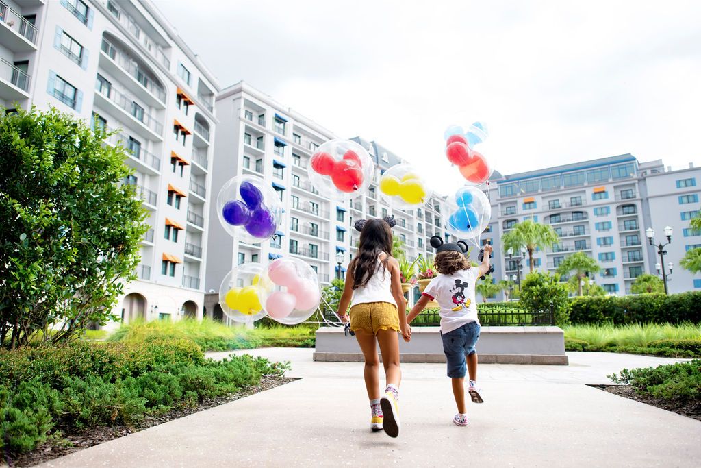 Two people running through a resort courtyard holding colorful balloons.