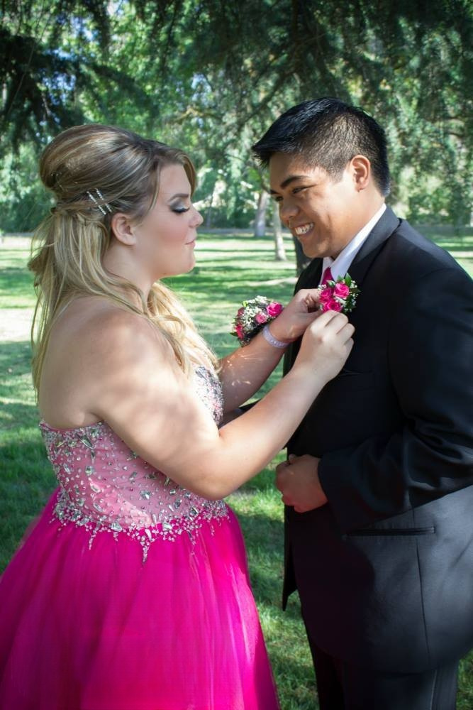 A young couple before prom, woman pins boutonniere to man's jacket lapel.