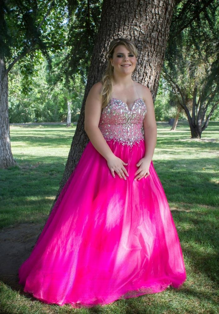 A young woman poses by a tree in a hot pink gown before her prom.