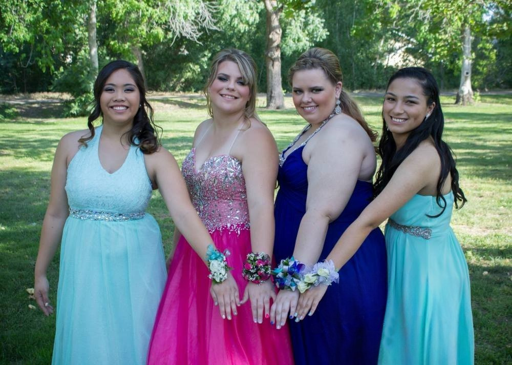 Four young women pose in their formal gowns and show off their corsages before the prom.