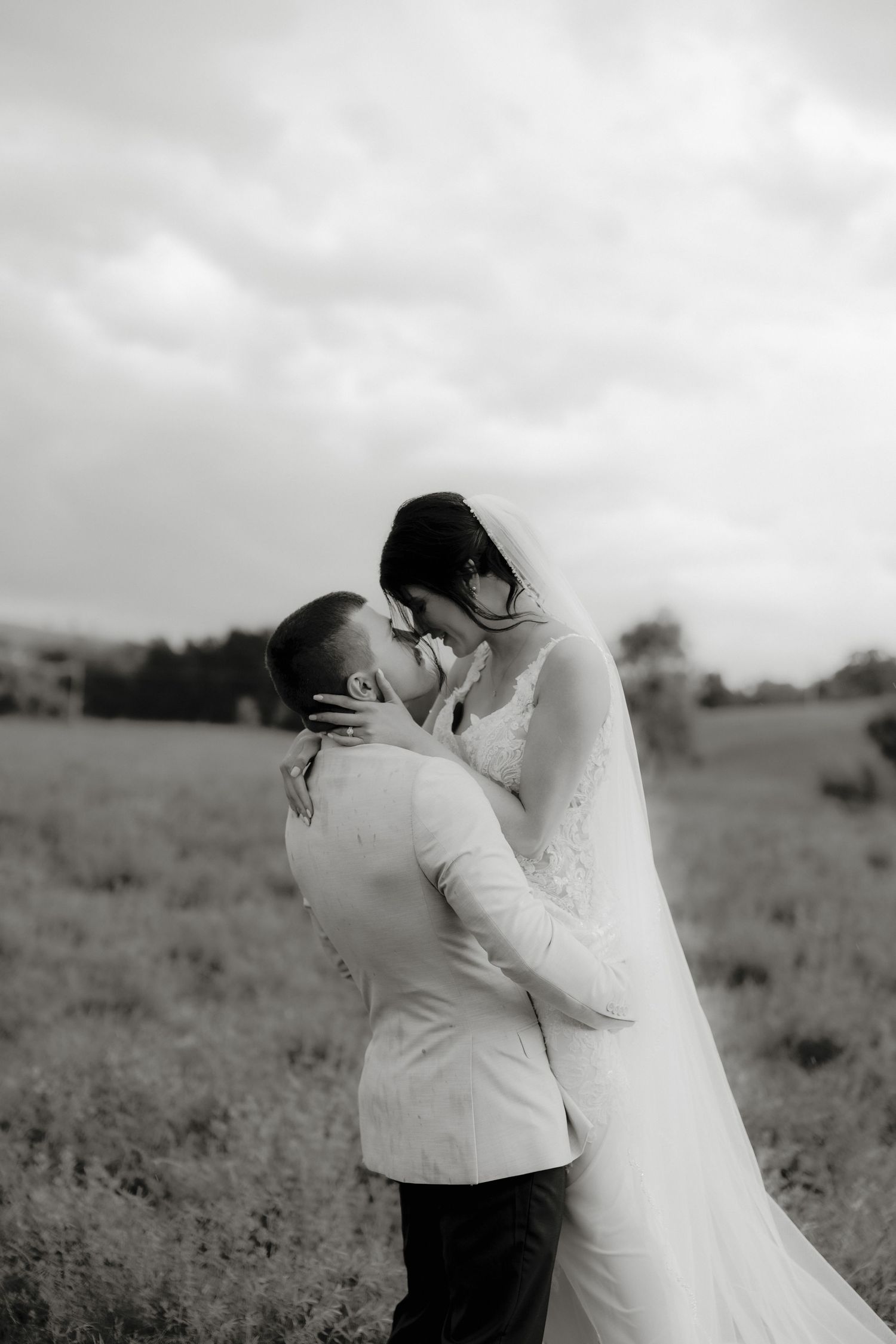 Black and white photo of a bride and groom sharing a romantic kiss in an open field on their wedding day.