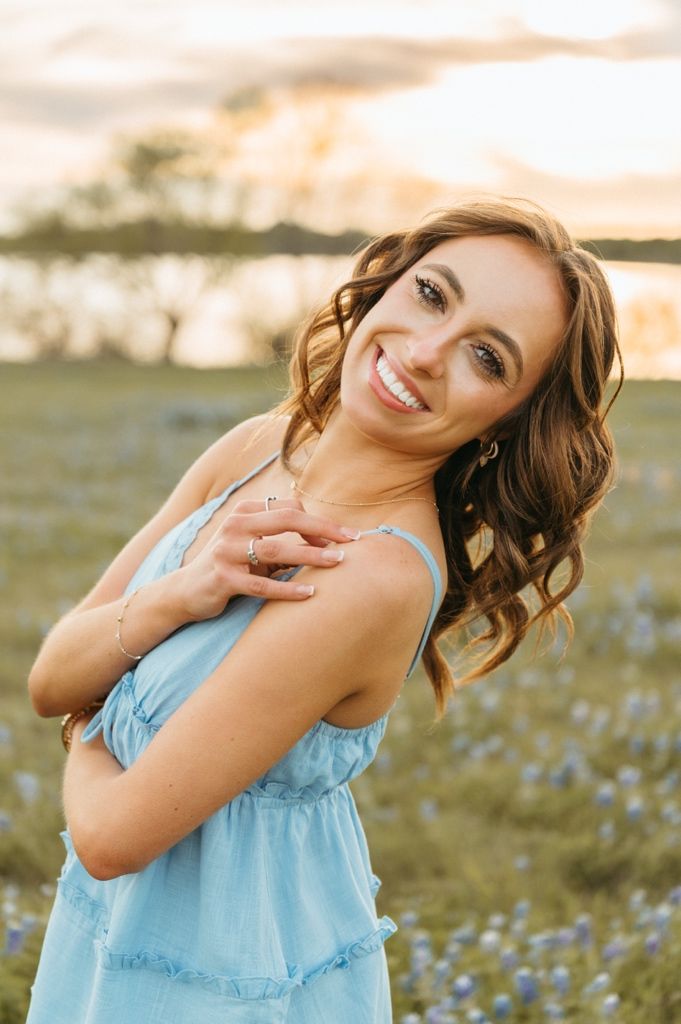 Young woman in blue sundress smiling in bluebonnet field at golden hour sunset.