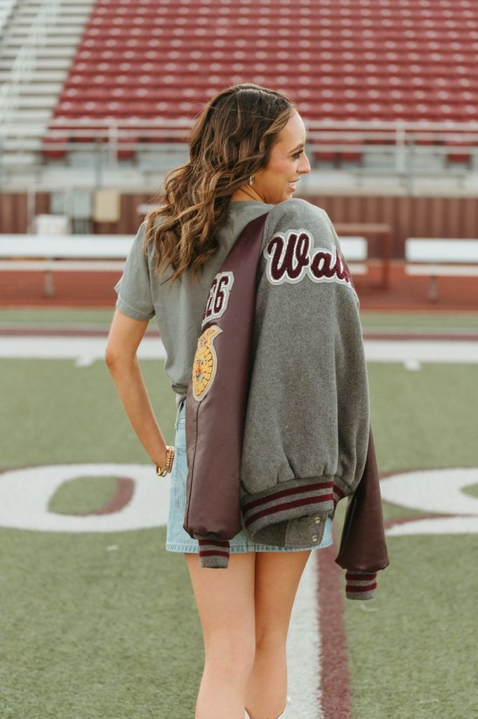 Young woman on football field holding a maroon and gray varsity letterman jacket over her shoulder.