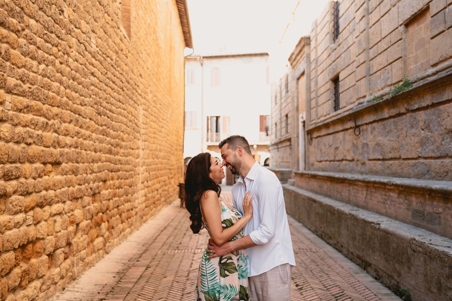 Couple sharing a romantic moment in a narrow cobblestone alley between ancient stone walls in Pienza , Tuscany