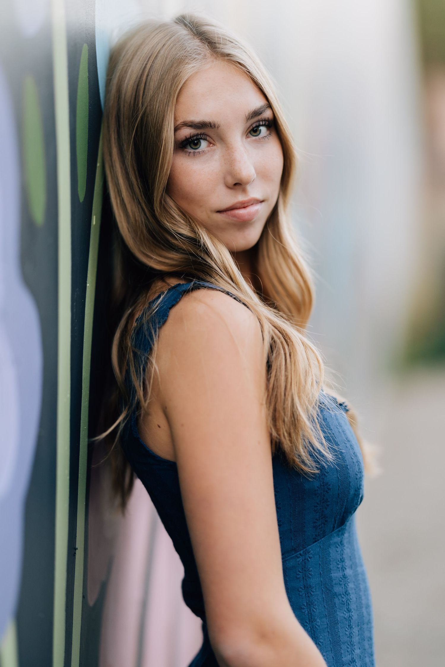 Young blonde woman in navy dress leaning on black iron railing, gazing upward thoughtfully outdoors.
