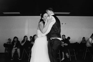 Bride and groom share their first dance embracing closely while wedding guests watch in black and white.