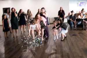 Blurred motion photo of wedding guests scrambling to catch the bouquet toss on a dance floor.