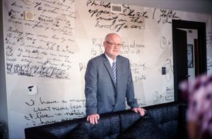Man in suit stands before a wall covered in handwritten text in a candid portrait.