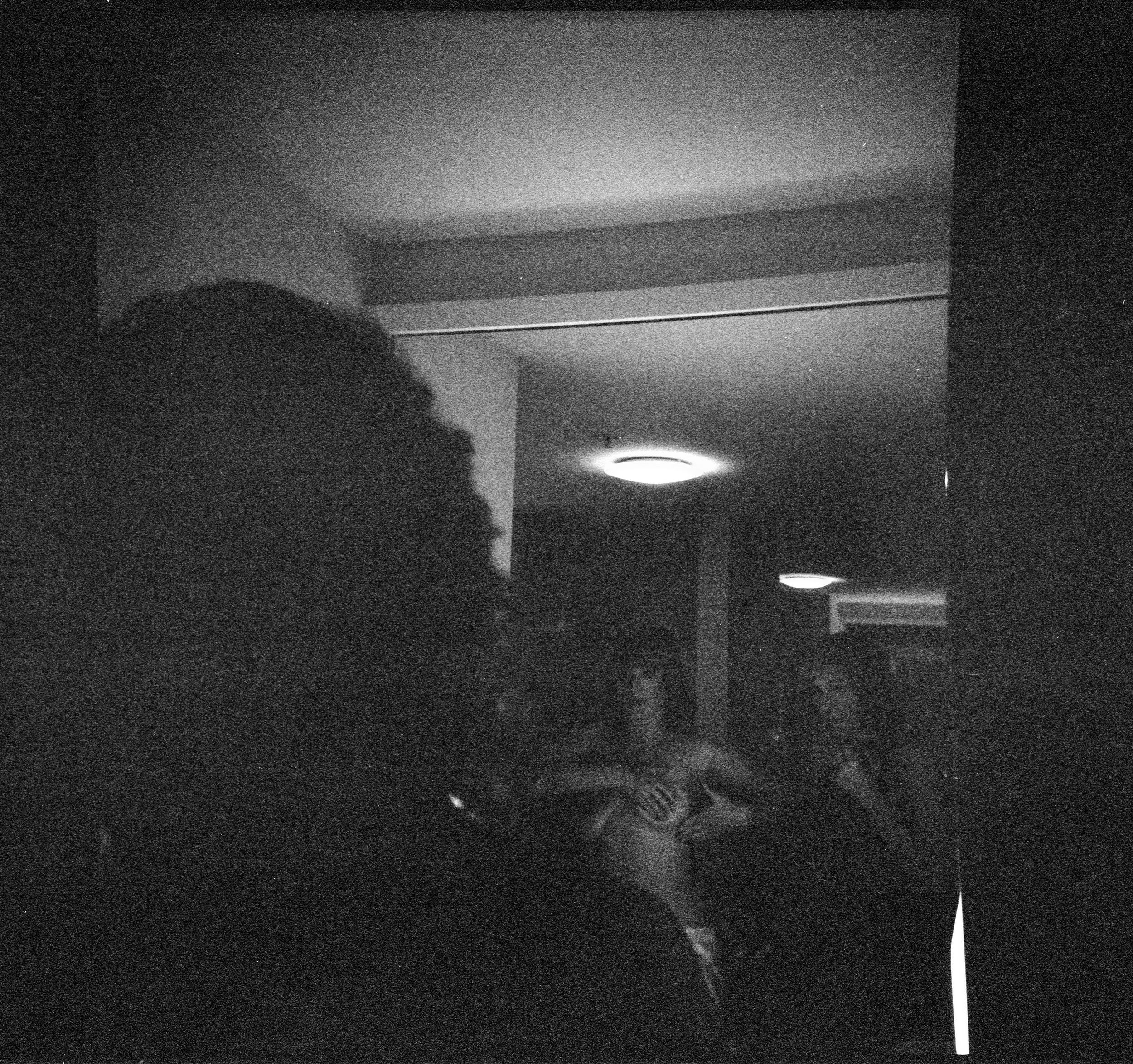 Dark grainy black and white photo of people gathered in a dimly lit room.