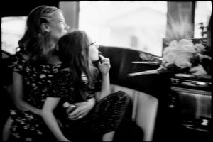 Mother and young daughter share a joyful moment together inside a vintage car in black and white.