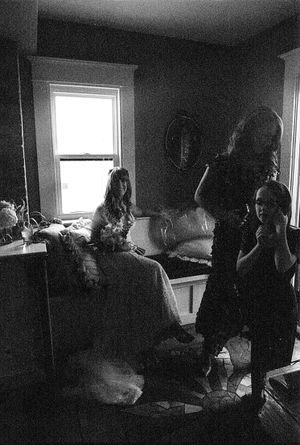 Black and white photo of women in a dimly lit bedroom near a bright window.