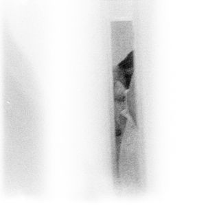 Minimalist black and white photo of a person partially visible through a narrow doorway.