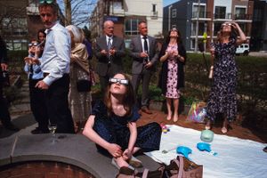 Group of people wearing eclipse glasses looking up at the sky outdoors during a solar eclipse event.