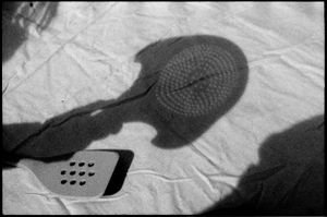 Black and white shadow photo of a spatula and hat casting shadows on a white cloth surface.