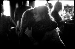 Black and white photo of two people sharing an intimate embrace at a dimly lit social gathering.