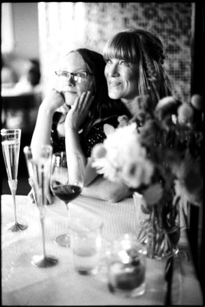 Two women sitting at a table with wine glasses and flowers in black and white.