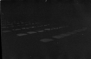 Dark black and white photo of rows of empty chairs set up for an outdoor event.