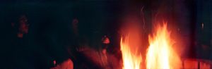 People gathered around a glowing campfire in a dark outdoor night setting.